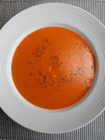 Overhead of red pepper and tomato soup in a white rimmed bowl on a ribbed grey placemat