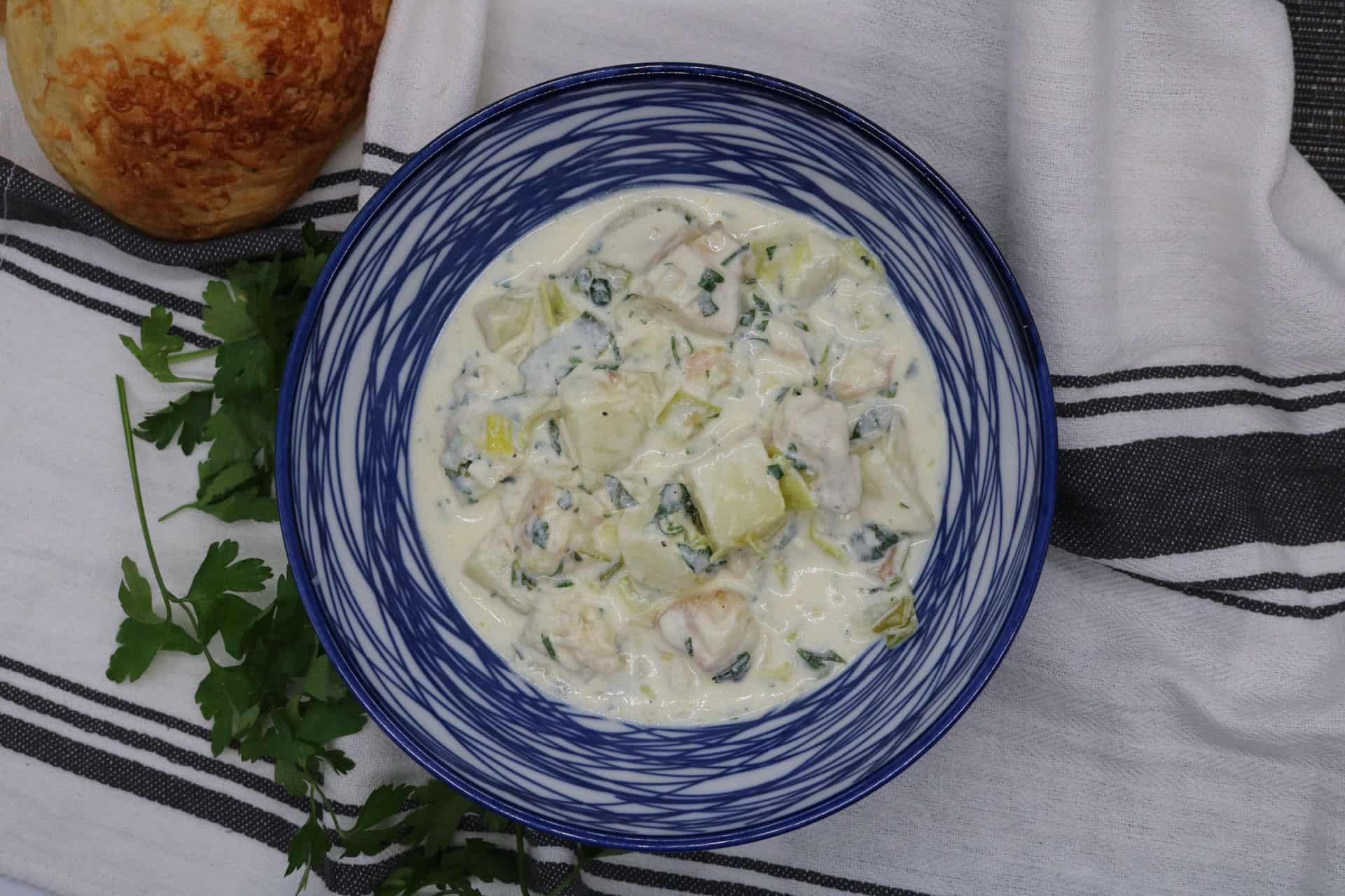 Portion of cullen skink in a blue and white bowl with bread on the side