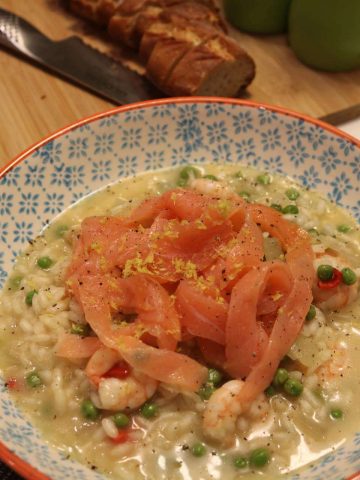 Bowls of risotto and a wooden board with sliced baguette and bread knife