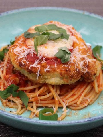 Turkey parmigiana with spaghetti in tomato sauce in turquoise bowl and fork