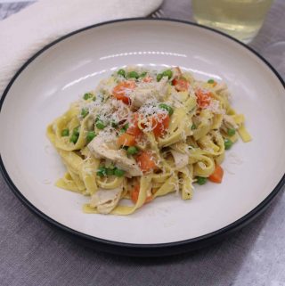 Creamy chicken and vegetable tagliatelle in a pasta bowl with glass of white wine and fork on the side
