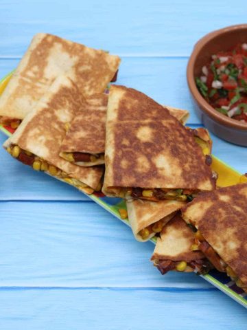 Assembled quesadillas cut into quarters on long slim serving platter, salsa and sour cream in terracotta dishes on the side
