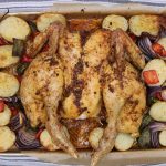 Cooked Spanish spatchcock chicken and vegetables on baking tray