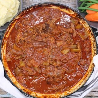 Overhead of bloody mary beef in large casserole with bowls of mashed potatoes and vegetables on the side