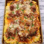Side view of smoky meatballs with cheesy polenta on baking tray with serving spoon