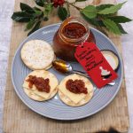 Jar of bacon and cranberry jam on grey dinner plate with water biscuits and cheese