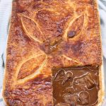 Easy steak pie in a white serving dish with a portion of pastry removed