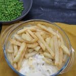 Fish and chip pie in a round glass serving bowl plus a bowl of peas on the side