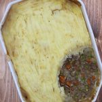 Shepherd's pie in a white serving dish with a portion of potatoes removed