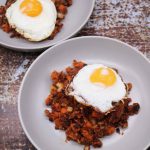 Two grey bowls with corned beef hash topped with a fried egg