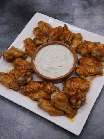 Buffalo chicken wings on square serving platter with blue cheese dip