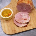 Honey roast gammon sliced on wooden board with bowl of piccalilli