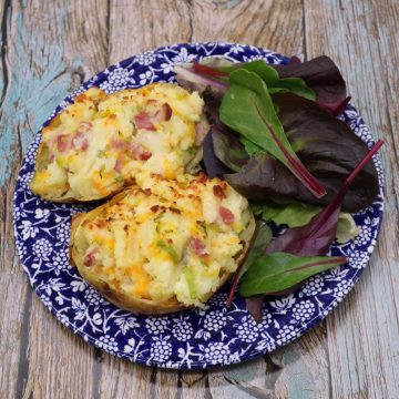 Leek, bacon and cheese baked potato on blue and white plate with salad leaves
