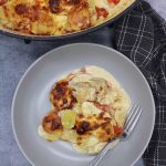 Creamy gratin of smoked haddock, tomatoes and potatoes grey bowl with fork beside oval casserole dish