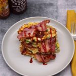 Sweetcorn, feta and spring onion pancakes with bacon and sriracha on grey plate