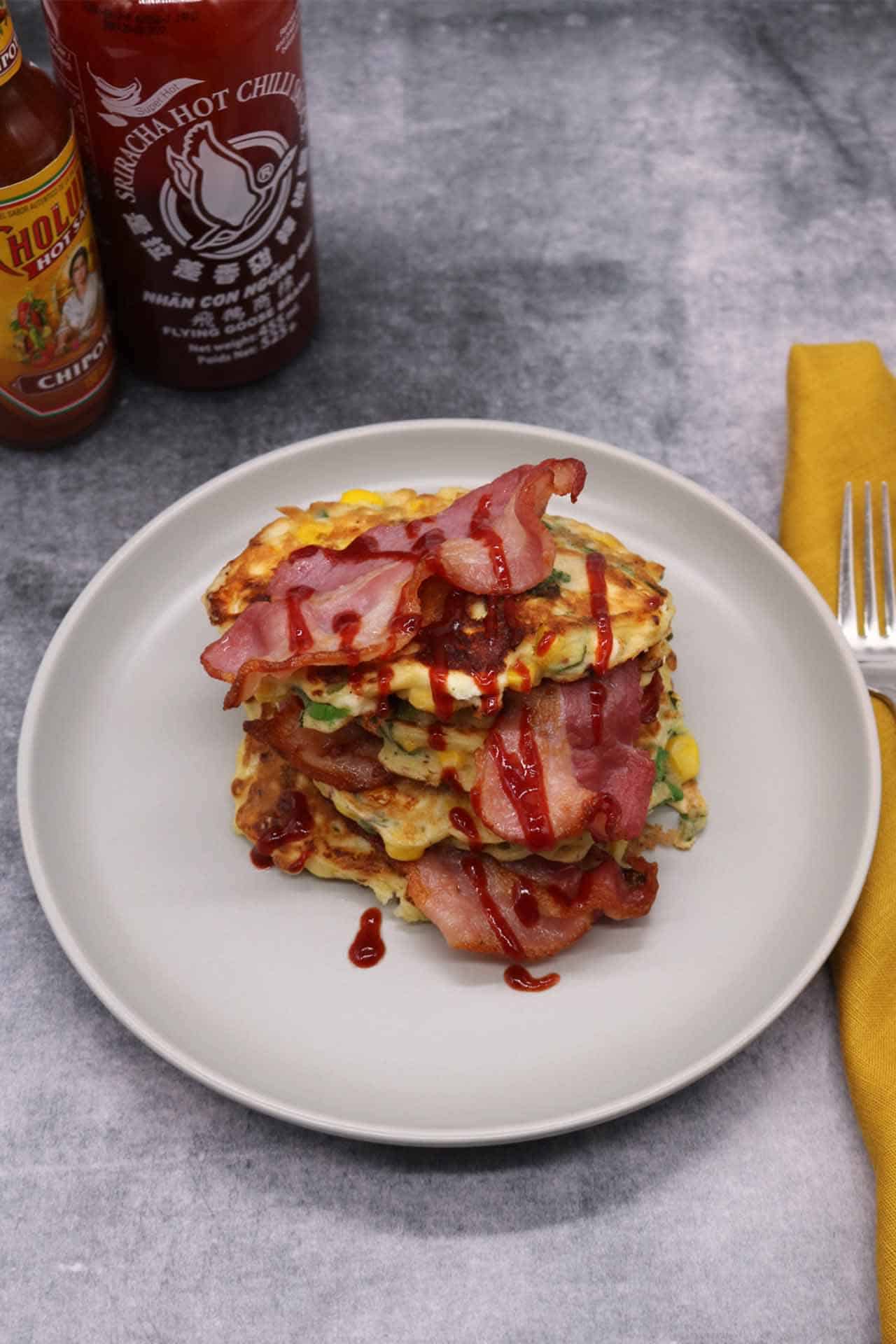 Sweetcorn, feta and spring onion pancakes with bacon and sriracha on grey plate