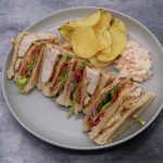 Club sandwich with crips and coleslaw on grey plate