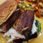 Close up of Pork belly slices inside bun with coleslaw and dirty fried on yellow plate