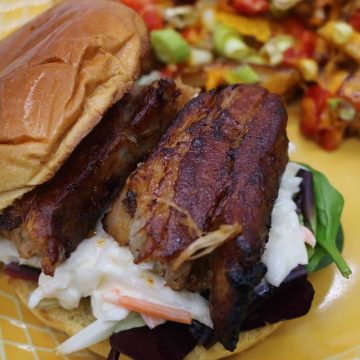 Close up of Pork belly slices inside bun with coleslaw and dirty fried on yellow plate