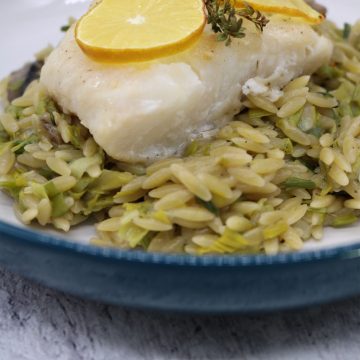 Baked cod with creamy orzo in bowl with lemon slice and thyme on top