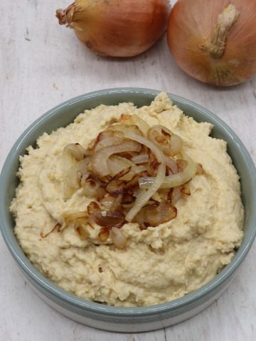 Caramelised onion houmous in bowl with onions on top and raw onions in background