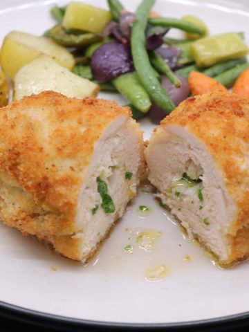 Chicken kiev on plate cut in two with vegetables in background