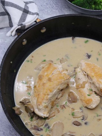 Creamy mushroom chicken in frying pan with broccoli in bowl in background