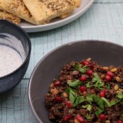 Lebanese lamb in bowl scattered with pomegranate seeds and herbs and flat breads on plate behind