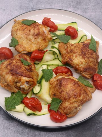 Paprika chicken thighs on plate with tomato and slices of cucumber
