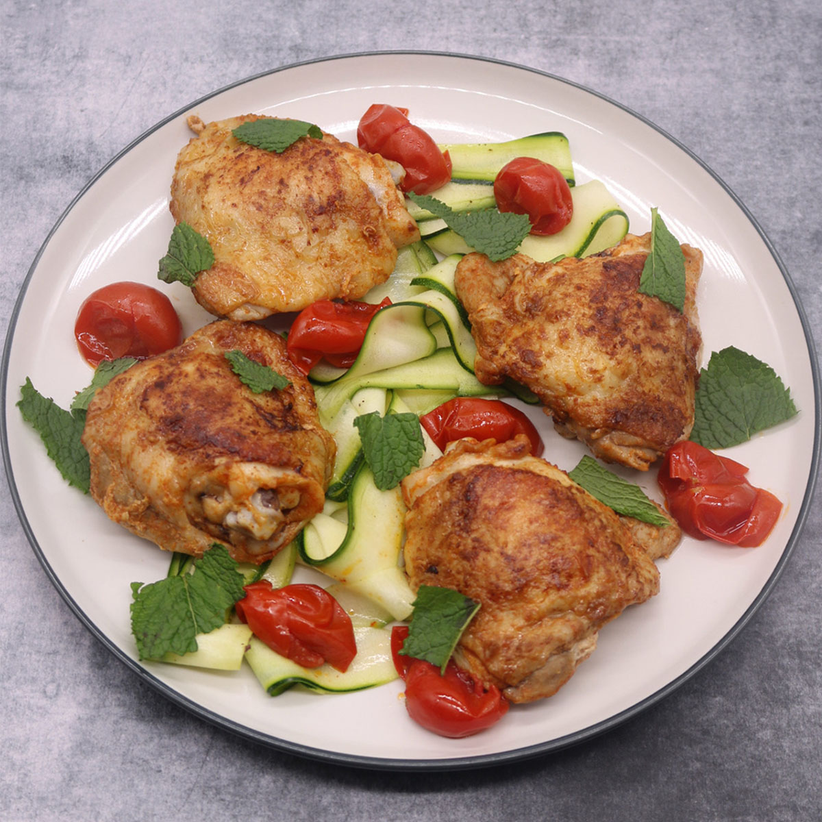 Paprika chicken thighs on plate with tomato and slices of cucumber