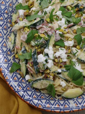 Pasta with bacon courgette and herbs on oval serving platter scattered with basil leaves