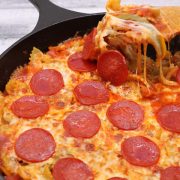 Pepperoni pizza pasta in skillet with wooden spoon removing portion