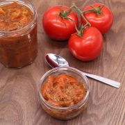 Spicy tomato relish in jar and small bowl with tomatoes and spoon on wooden board