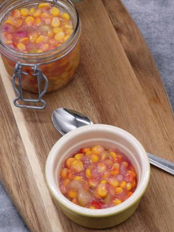 Sweetcorn relish in jar and small bowl on wooden board with spoon