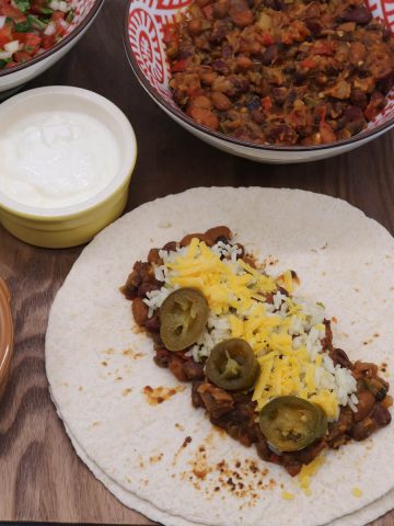 Veggie chilli on flour tortilla with rice jalapeños and cheese on wooden board