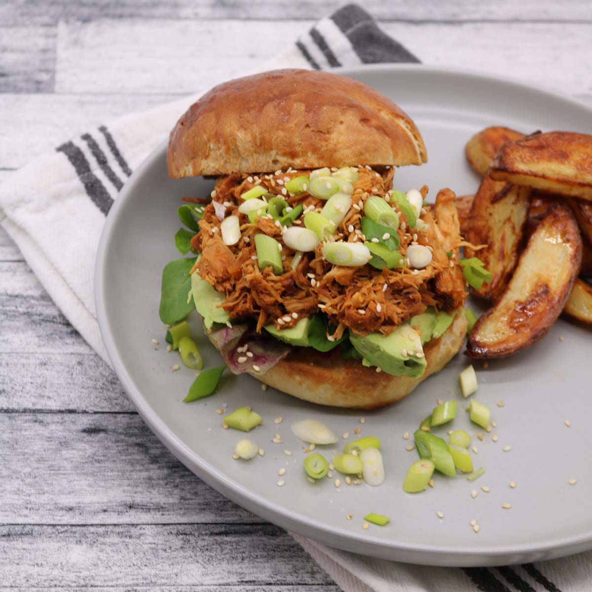 Slow cooker korean pulled chicken on a brioche bun with spring onions avocado sesame seeds and chunky chips