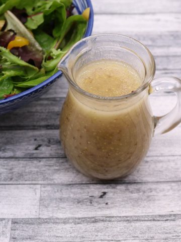 Honey mustard dressing in clear jug with salad in blue and white bowl