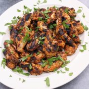 Tandoori chicken wings on oval white platter scattered with coriander