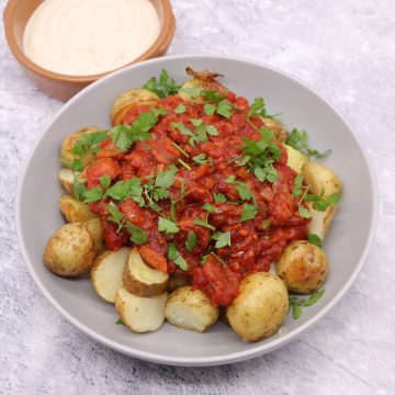 Chorizo patatas bravas in grey bowl with dipping sauce