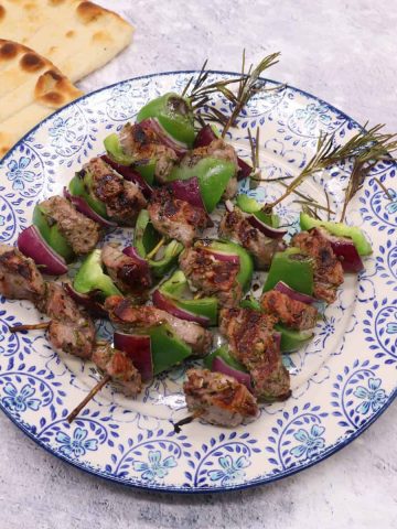Lamb and rosemary skewers on blue and white plate with flat breads