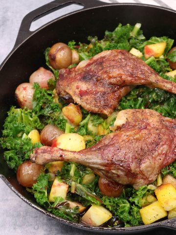 Duck legs in blackberry and port sauce in skillet with kale onions and potatoes