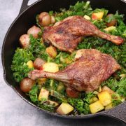 Duck legs in blackberry and port sauce in skillet with kale onions and potatoes