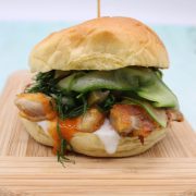 Piri piri crispy chicken in bun with cucumber sitting on wooden board