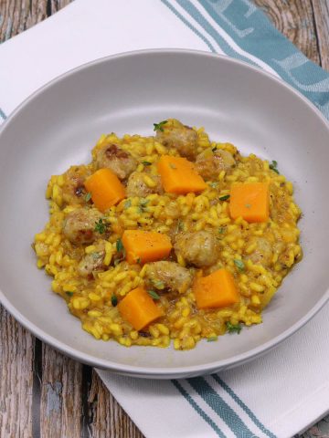 Sausage and squash risotto in grey bowl with green and white towel