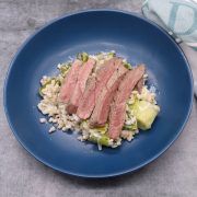 Lamb steaks and leek barley risotto in a blue bowl