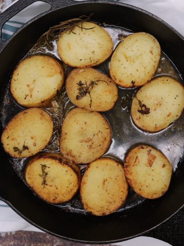 Buttery herbed melting potatoes in skillet with rosemary and thyme