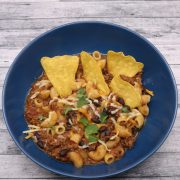 Slow cooker cheesy chilli mac in a blue bowl with tortilla crisps