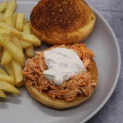 Slow cooker buffalo chicken on a bun with chips tin a grey plate