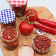 Chilli jam in jars with tomato and red chillis on wooden board