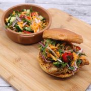 Satay chicken burger in a bun with bowl of crunchy slaw on wooden board